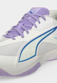 Άσπρα και γκρι αθλητικά παπούτσια Puma με ανοιχτόμωβ κορδόνια και σόλα, με λογότυπο με μπλε περίγραμμα και υφασμάτινο επάνω μέρος με υφή.