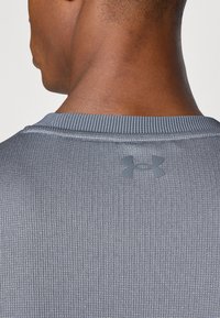 Gray athletic shirt featuring a textured fabric, ribbed collar, and a small logo on the back. The design is simple and functional.