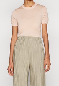 Světlý růžový pletený top s krátkým rukávem a kulatým výstřihem, který je spárován s vyššími skládacími kalhotami olivově zelené barvy. Viditelný hladký texturový detail.