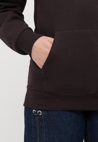 Hanorac maro cu un buzunar frontal, manșete și tiv ribate; combinat cu blugi de un albastru închis cu accente metallic.