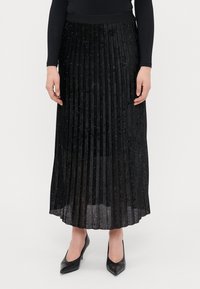 Sort plisseret nederdel i et struktureret stof, prydet med små paljetter; parret med sorte spidse hæle.