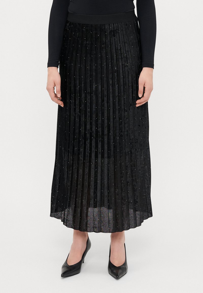 Sort plisseret nederdel i et struktureret stof, prydet med små paljetter; parret med sorte spidse hæle.