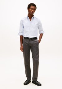 Camisa azul clara às riscas com botões, mangas arregaçadas, combinada com calças cinzentas e sapatos de couro pretos. Design simples e elegante.