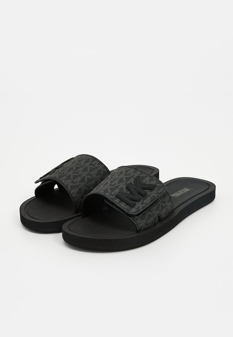 Chanclas negras con parte superior de tela texturizada que presenta un patrón geométrico y un logotipo "MK" en relieve. Suela de goma para mayor comodidad.