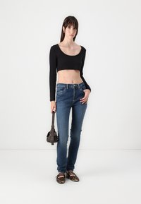 Black cropped long-sleeve top, blue fitted jeans, and animal-print flats; holding a small brown bag with a shoulder strap.
