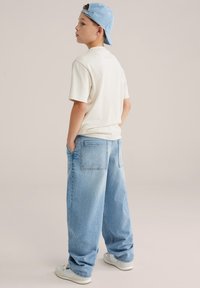 Kreemjas t-särk kombineeritud helesiniste lahtiste teksadega. Riietus on vabaaja stiilis ja lihtsa nokamütsiga. Välimuse lõpetavad valged jalatsid.