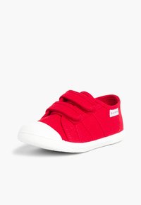 Zapato de tela roja con suela de goma blanca, que cuenta con dos correas de Velcro, una punta redondeada y un cuerpo texturizado con acentos de costura.