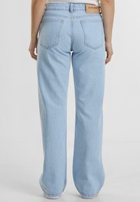 Lyseblå vid ben jeans med høy midje, som har to baklommer og et lærmerke i midjen. Laget av bomullsstoff med en strukturert finish.