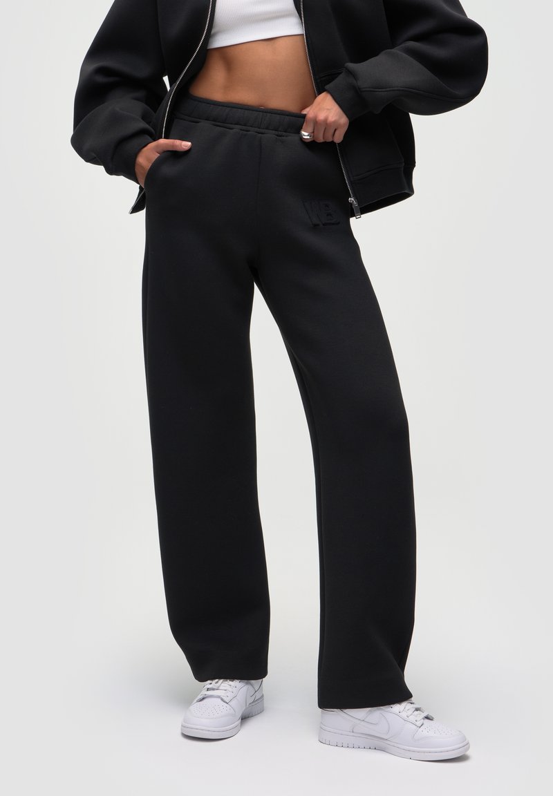 Sorte sweatpants i afslappet pasform med elastisk talje og prægede logo. Sammen med hvide sneakers på en neutral baggrund.