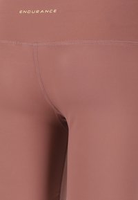 Kirefitting leggings w kolorze przygaszonego mauve, z gładką teksturą i subtelnym złotym logo na pasku.