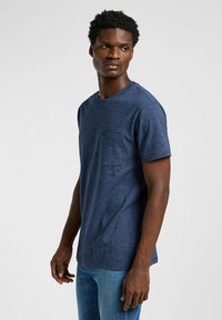 Mörkblå bomullströja med rund halsringning, korta ärmar och en bröstficka på vänster sida. Slät textur, avslappnad passform.