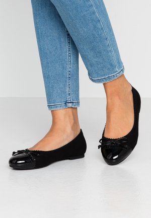 Fødder iført lyseblå denimjeans og sorte balletsko med skinnende tåhætte og små dekorative sløjfer.