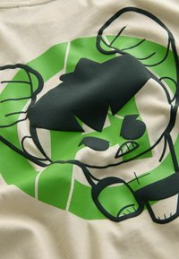 Lichtbeige T-shirt met een groen-zwart grafisch ontwerp van een cartoonfiguur met gespierd postuur en een boze uitdrukking.