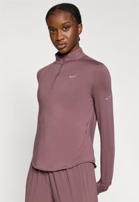 Αθλητικό τοπ με μακριά μανίκια και φερμουάρ, σε απαλή μωβ απόχρωση. Διαθέτει μικρό λογότυπο Nike σε ασημί και διακριτικές λεπτομέρειες στα πλάγια των μανικιών.