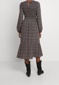Langärmliges Kleid mit enganliegendem, gerafftem Oberteil, knielangem Rock, Blumenmuster in Lila und Creme sowie einem Schlüsselverschluss auf der Rückseite. Tragen mit schwarzen Stiefeln.