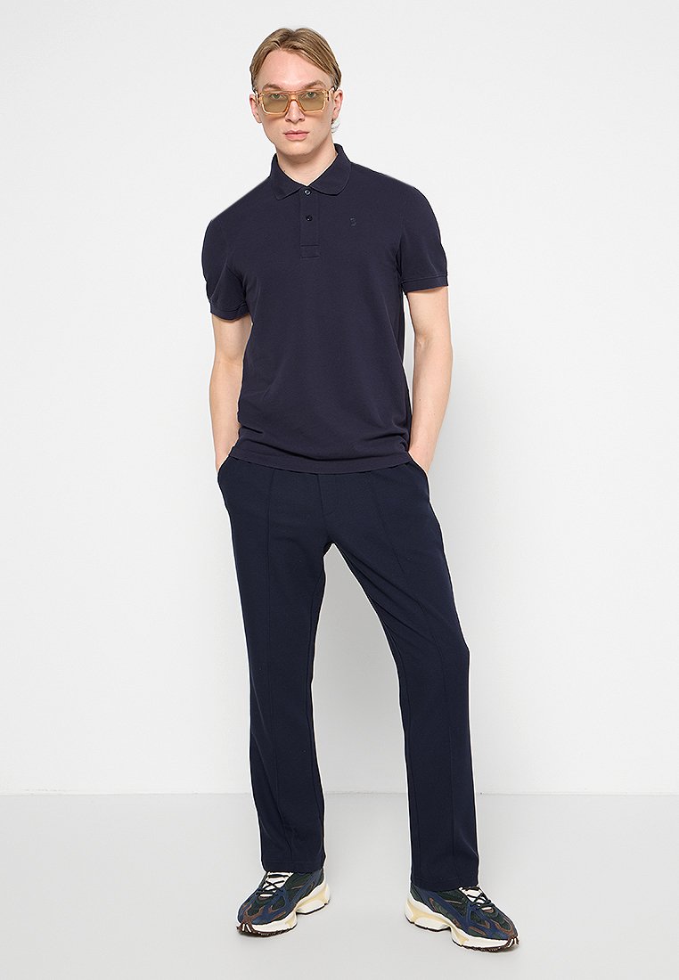 Navy-Polohemd mit kurzen Ärmeln, klassischem Kragen und dezentem Logo; kombiniert mit marineblauen Hosen und gemusterten Sneakern für einen abgestimmten Look.