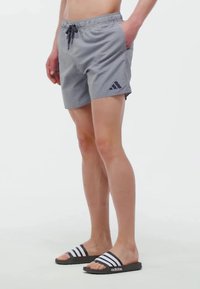 Pánske plavky v modro-bielom pruhovanom dizajne, s elastickým pásom a šnúrkou; na ľavej strane sa nachádza logo.