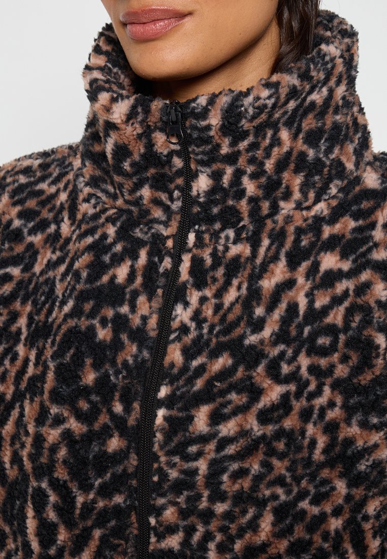 Chaqueta de forro polar con estampado de leopardo en negro, marrón y crema. Cuenta con un cuello alto y cierre frontal con cremallera. Textura suave y corte relajado.