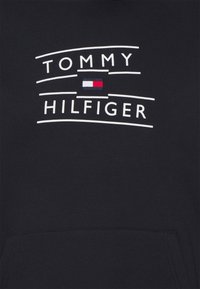 Czarna bluza z kapturem z logo "TOMMY HILFIGER" w białym kolorze, z małym prostokątnym akcentem w kolorach czerwonym, białym i niebieskim. Miękka tkanina bawełniana.