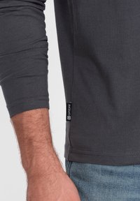 Langärmliges graues T-Shirt aus Baumwolle, mit schmalem Schnitt, umgeschlagenen Ärmeln und einem vertikalen schwarzen Etikett an der Seitennaht.