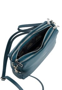 Teal Leder Umhängetasche mit zwei Reißverschlussfächern, silbernem Zubehör und einer strukturierten Außenseite. Das Innere verfügt über ein schwarzes Futter.