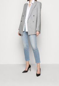 Blazer gris de doble botonadura con hombros estructurados, usado sobre una camisa blanca de botones, combinado con jeans ajustados de color azul claro y tacones negros puntiagudos.