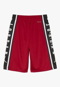 Pantalones cortos deportivos rojos con un panel lateral negro que presenta detalles blancos y la marca "JORDAN". Hechos de una tela texturizada, con una cinturilla elástica.