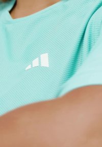 Ljus turkosa mesh sporttröja med vita logodetaljer. Texturen är andningsbar, med rundad hals och korta ärmar.