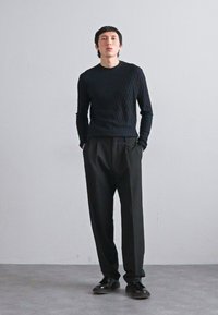 Schwarzes strukturiertes Strickoberteil mit langen Ärmeln, kombiniert mit lockeren schwarzen Hosen und schwarzen Schuhen. Einfache, moderne Gestaltung mit minimalen Akzenten.