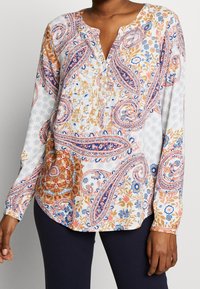 Blouse à manches longues boutonnée en blanc avec un motif cachemire multicolore. Comprend des accents bleus, orange et floraux ; tissu léger.