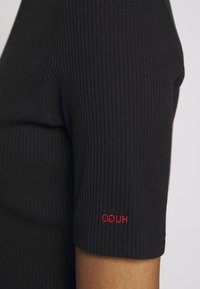 Czarna, prążkowana koszulka z krótkim rękawem, z czerwonym haftowanym logo "HUGO" na rękawie. Gładka faktura, dopasowany krój.