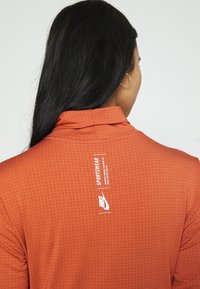 Orange långärmad skjorta med ett strukturerat rutmönster, med krage och en Nike-logotyp samt märkning vid baksidan av halsen.