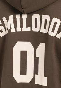 Brązowa bluza z kapturem z dużymi białymi literami blokowymi, na których widnieje "SMILODON" oraz numer "01" na plecach, wykonana z miękkiego materiału.