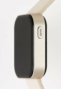 Smartwatch met een zwart rechthoekig scherm, gouden metalen rand en een crèmekleurige siliconen band. Heeft een prominente zijknop met het label "SPRT."