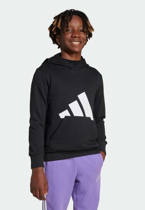 Haut à capuche noir avec un grand logo Adidas blanc, doté d'une poche kangourou et de poignets côtelés. Associé à un pantalon de jogging violet clair.
