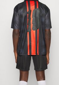 Camiseta de fútbol negra con rayas verticales rojas, que presenta un gran "18" en la parte trasera. Fabricada con material ligero y de textura suave.