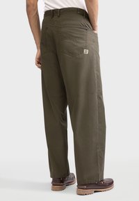 Pantalones chinos holgados color verde oliva con pierna recta, bolsillos traseros y una textura sutil. Presentan un lazo para cinturón y un cierre con un solo botón.