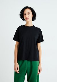 Zwart katoenen t-shirt met korte mouwen en ronde hals, gecombineerd met groene relaxte broek. Eenvoudig, effen ontwerp.