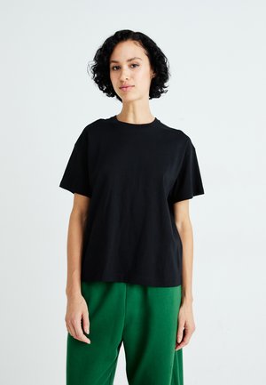Zwart katoenen t-shirt met korte mouwen en ronde hals, gecombineerd met groene relaxte broek. Eenvoudig, effen ontwerp.