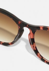 Óculos de sol tartaruga com acabamento brilhante, lentes em gradiente castanho e um design distinto com recortes nas armações.