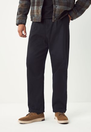 Sorte bomuld bukser med en afslappet pasform, kombineret med brune ruskindssko. Outfit'et inkluderer en ternet flannelskjorte i jordfarver.