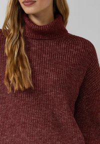 Bordowy golf z teksturowanej dzianiny o luźnym kroju i prążkowanym kołnierzu. Projekt charakteryzuje się subtelnymi różnicami w odcieniach koloru.