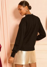 Maglione nero con maniche lunghe, polsini a coste e un collo texture, abbinato a una gonna dorata lucida.