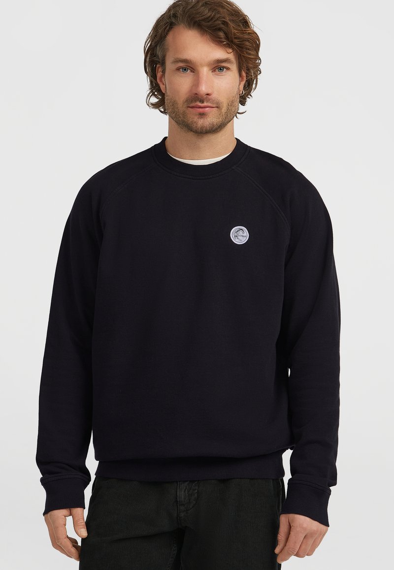 Zwarte sweater met ronde hals, gemaakt van zachte stof, met raglanmouwen, ribgebreide manchetten en een klein cirkelvormig logo op de borst.