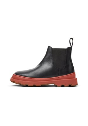 Bottine Chelsea en cuir noir avec semelle épaisse en caoutchouc rouge, languette de traction à l'arrière, panneau élastique latéral et semelle à crampons robustes.