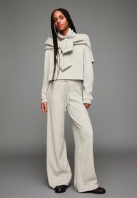 Ljust grå tvådelad outfit som består av en kortärmad ribbad tröja och vida byxor med dragsko, som visar upp en strukturerad stickad textil.