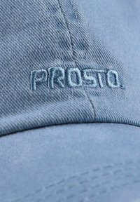 Niebieska czapka wykonana z fakturowanej tkaniny z haftowanym logo "PROSTO." w jaśniejszym odcieniu. Widoczne detale szwów i przeszyć na daszku.