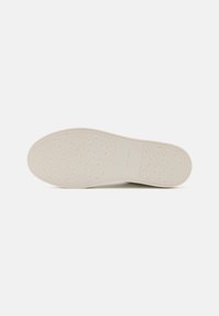 Suola di scarpa in gomma color crema con una texture a motivi, caratterizzata da loghi ripetuti e un bordo liscio. Progettata per aderenza e stabilità.