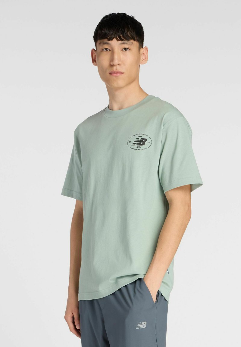 Mint green cotton t-shirt with short sleeves, round neckline, and a black logo on the chest. Paired with gray athletic shorts.