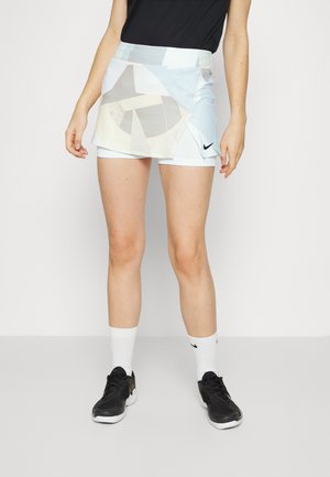 Jupe de sport pour femmes Nike, bleu clair avec des accents de motif géométrique. Elle présente une taille haute et des shorts internes. Baskets noires et chaussettes blanches.
